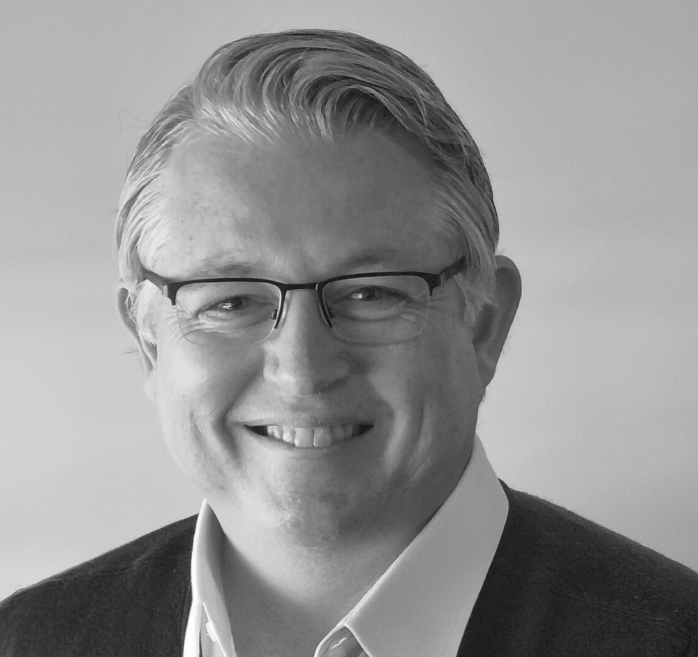 A black and white photo of a man wearing glasses and a sweater.